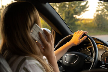 Happy young woman speaking by mobile phone while driving car. Business woman talking phone call in automobile. Unsafely risky driving. Concept of multitasking 