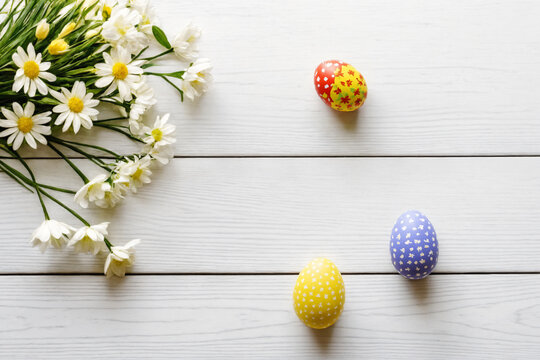 Flatlay photo of Easter eggs with spring flowers on a white wooden surface