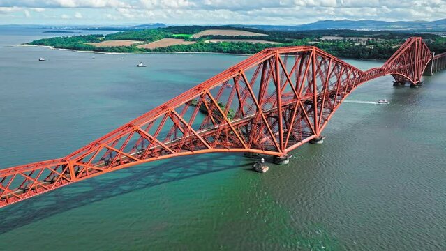 Aerial view of Forth Bridge, a long red railway bridge crossing the Forth estuary. Cantilever railway bridge carrying passengers and freight, cruise ship transporting tourists in Scotland.