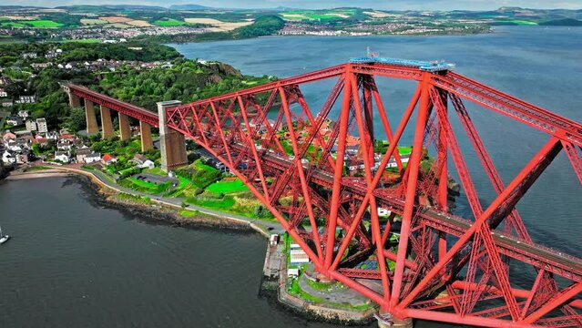 Aerial view of Forth Bridge, a long red railway bridge crossing the Forth estuary. Cantilever railway bridge carrying passengers and freight, cruise ship transporting tourists in Scotland.