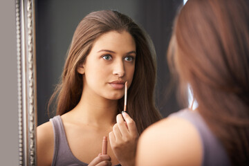 Woman, thinking and lip gloss in mirror for makeup, application and getting ready for wellness in bedroom. Mouth, shine and thoughtful person with cosmetics, beauty product and self care in home