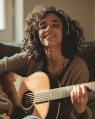 Portrait of a girl with curly hair and headphones playing the guitar. A happy young woman in...