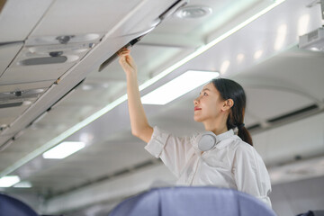 Asian female traveler putting luggage into overhead locker on airplane during boarding.