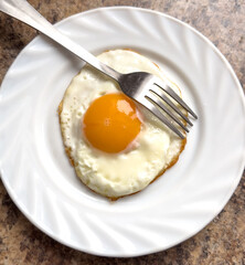 Fried egg on a white plate with a fork on the table