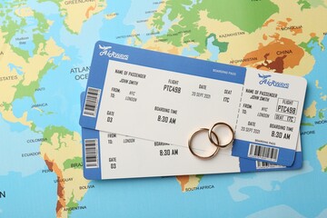 Honeymoon concept. Plane tickets and golden rings on world map, top view