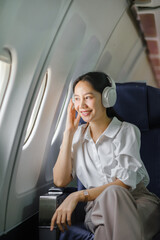 Asian woman sitting and using a smartphone in an airplane Listening to music next to the airplane seat window travel and technology concept