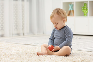 Children toys. Cute little boy playing with red ball on rug at home, space for text
