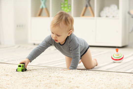 Children toys. Cute little boy playing with toy car on rug at home