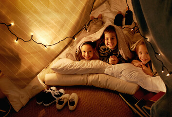 Children, smile and playing in blanket fort with portrait for fantasy, bonding and string lights at...