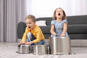 Little children pretending to play drums on pots at home