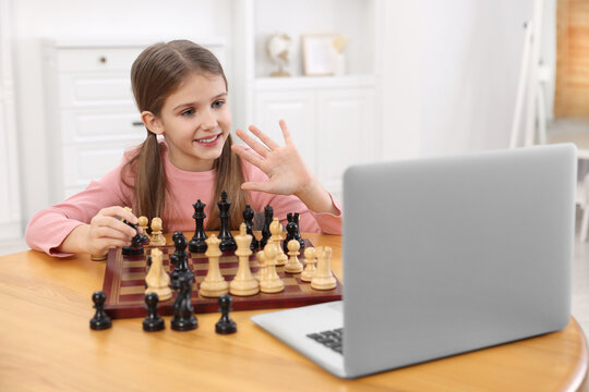 Cute girl learning to play chess with online tutor at home