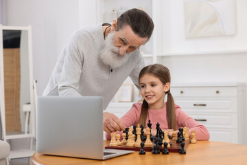 Grandfather teaching his granddaughter to play chess following online lesson at home