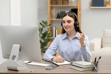 Fototapeta premium E-learning. Young woman taking notes during online lesson at table indoors