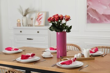 Color accent table setting. Plates, cutlery, pink napkins and vase with beautiful roses in dining...