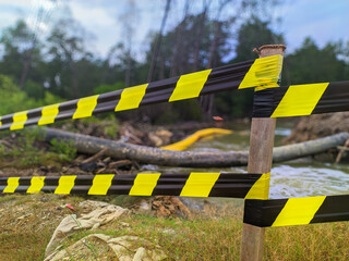 selective focus on yellow and black barricade tape with a blurry river background. concept of...