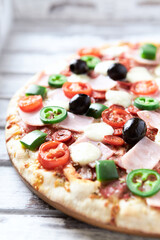 Pizza with ham, mozzarella cheese, cherry tomatoes, green and jalapeno pepper, black olives and fresh basil. Bright background. Close up	