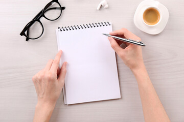 Woman with notebook and pen at white wooden table, top view. Space for text