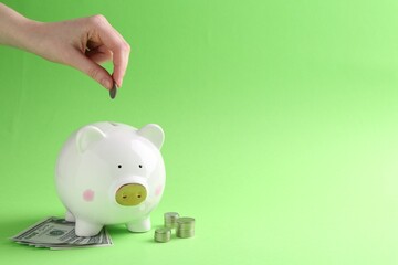 Financial savings. Woman putting coin into piggy bank on green background, closeup. Space for text