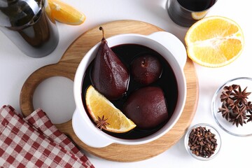 Tasty red wine poached pears in pot, orange and spices on white table, flat lay