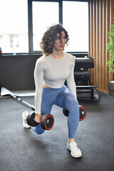 Young woman lifting the dumbbells in gym. Woman pumping up muscles with dumbbells