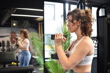 Young woman lifting the dumbbells in gym. Woman pumping up muscles with dumbbells