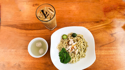 chicken noodles with meatball sauce plus green vegetables and lime on a white plate, a cup of iced milk coffee at the coffee shop