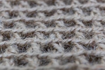 The texture of a hand-knitted jute rug with a repeating pattern of cells, photographed close up.