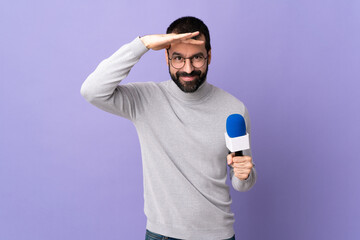 Adult reporter man with beard holding a microphone over isolated purple background looking far away...