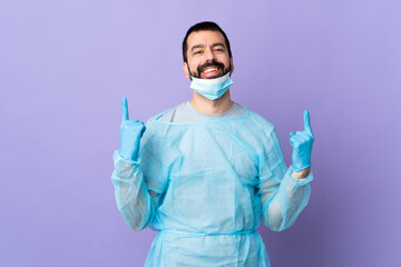 Surgeon man with beard with blue uniform over isolated purple background pointing up a great idea