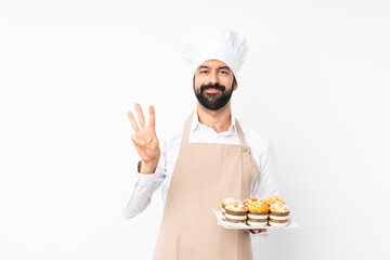 Young man holding muffin cake over isolated white background happy and counting three with fingers
