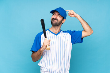 Young man playing baseball over isolated blue background having doubts while scratching head