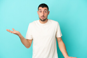 Fototapeta premium Young handsome caucasian man isolated on blue background making doubts gesture