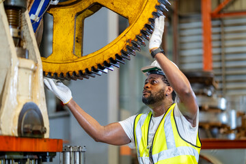 African American mechanic worker is checking the gear for hydraulic machine inside metal steel...