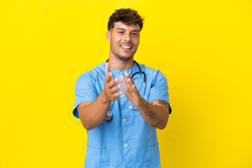 Young surgeon doctor man isolated on yellow background applauding after presentation in a conference