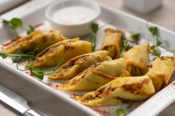 Delicious fried thin pancakes with meat and mushrooms on a white plate. Ukrainian cuisine