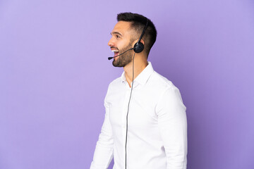 Telemarketer man working with a headset isolated on purple background laughing in lateral position