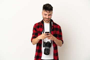 Young photographer caucasian man isolated on white background sending a message with the mobile