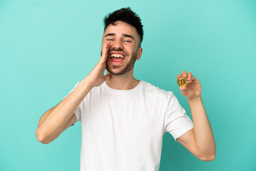 Young man holding a Bitcoin isolated on blue background shouting with mouth wide open