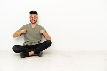 Young caucasian man sitting on the floor isolated on white background with surprise facial...