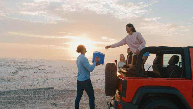 Young couple with friends on vacation unloading cool box from car at beach watching morning sunrise on road trip  - shot in slow motion