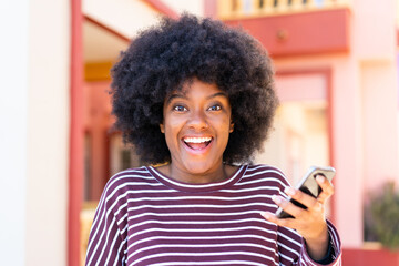 African American girl using mobile phone at outdoors with surprise and shocked facial expression