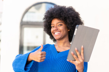 African American girl holding a tablet at outdoors with thumbs up because something good has...