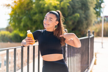 Young pretty sport woman holding an orange juice at outdoors with surprise facial expression