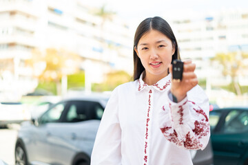 Young Chinese woman holding car keys at outdoors with happy expression