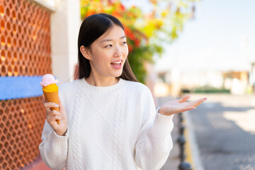 Pretty Chinese woman with a cornet ice cream at outdoors with surprise facial expression