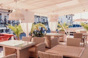 Wicker furniture tables in the open air are waiting for visitors. The interior of the restaurant in the open air. Empty tables of street cafe.