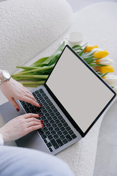 Top view of hands business woman sitting in armchair and working on laptop near bouquet of tulips and cup.