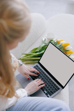 Top view of hands business woman sitting in armchair and working on laptop near bouquet of tulips and cup.