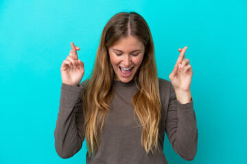 Young blonde woman isolated on blue background with fingers crossing