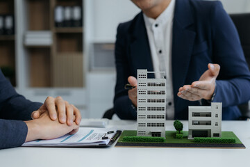 Real estate broker agent presenting and consult to customer to decision making sign insurance form agreement, home model, concerning mortgage loan offer in office.